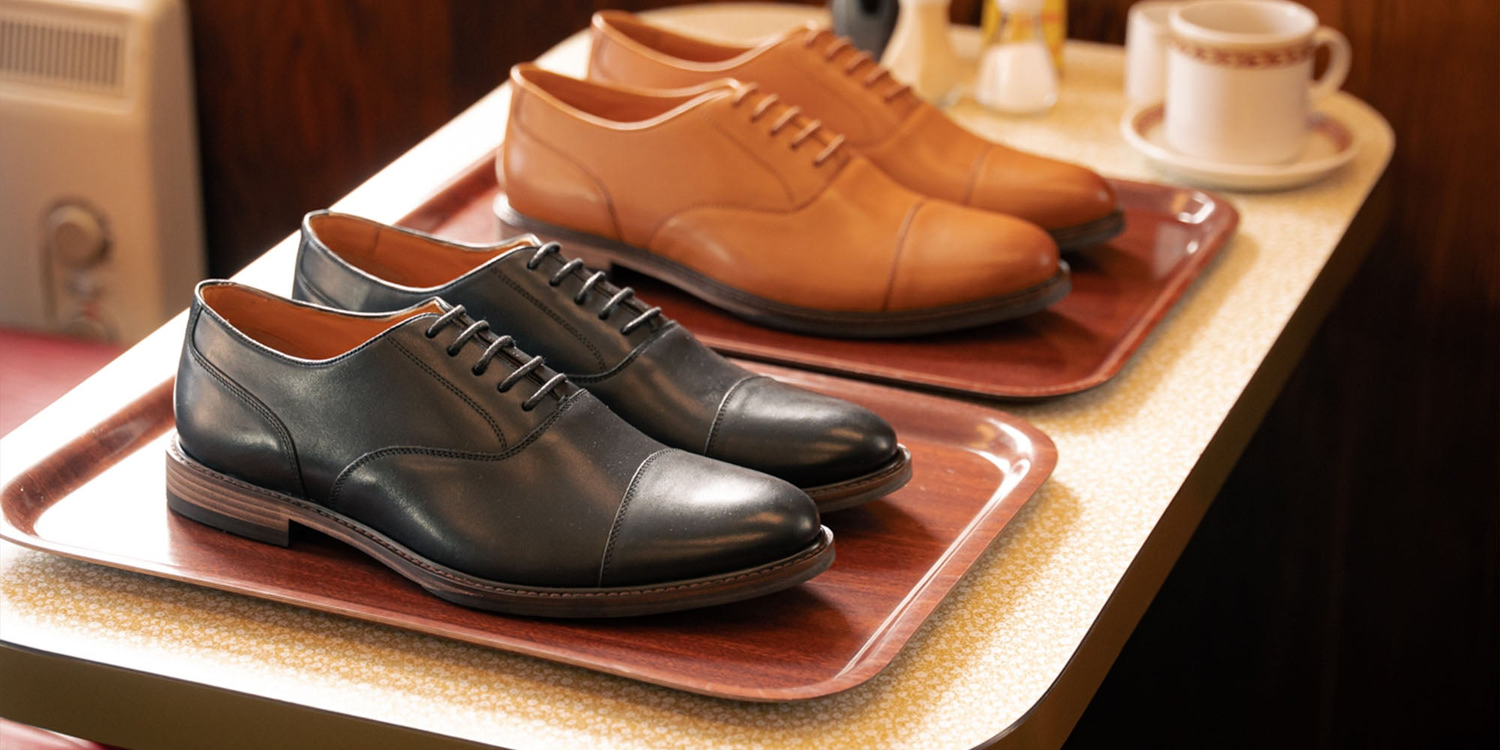 LANX grey, black and brown, derby and chelsea boots on a wooden shoe rack.